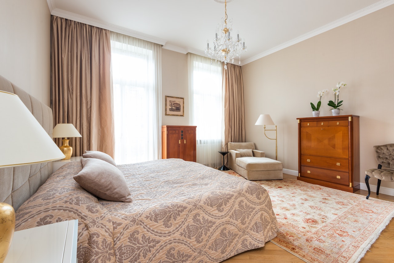 Charmingly decorated master bedroom with layers of cozy quilts, throw pillows, and morrocan rugs, with a few pieces of elegant furniture in the background.